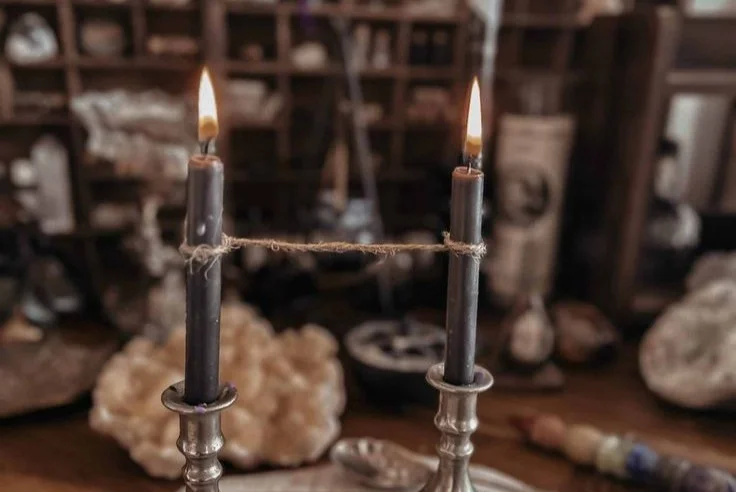 A single frayed cord lying loose on dark stone beside an unlit white candle, photographed in low warm light