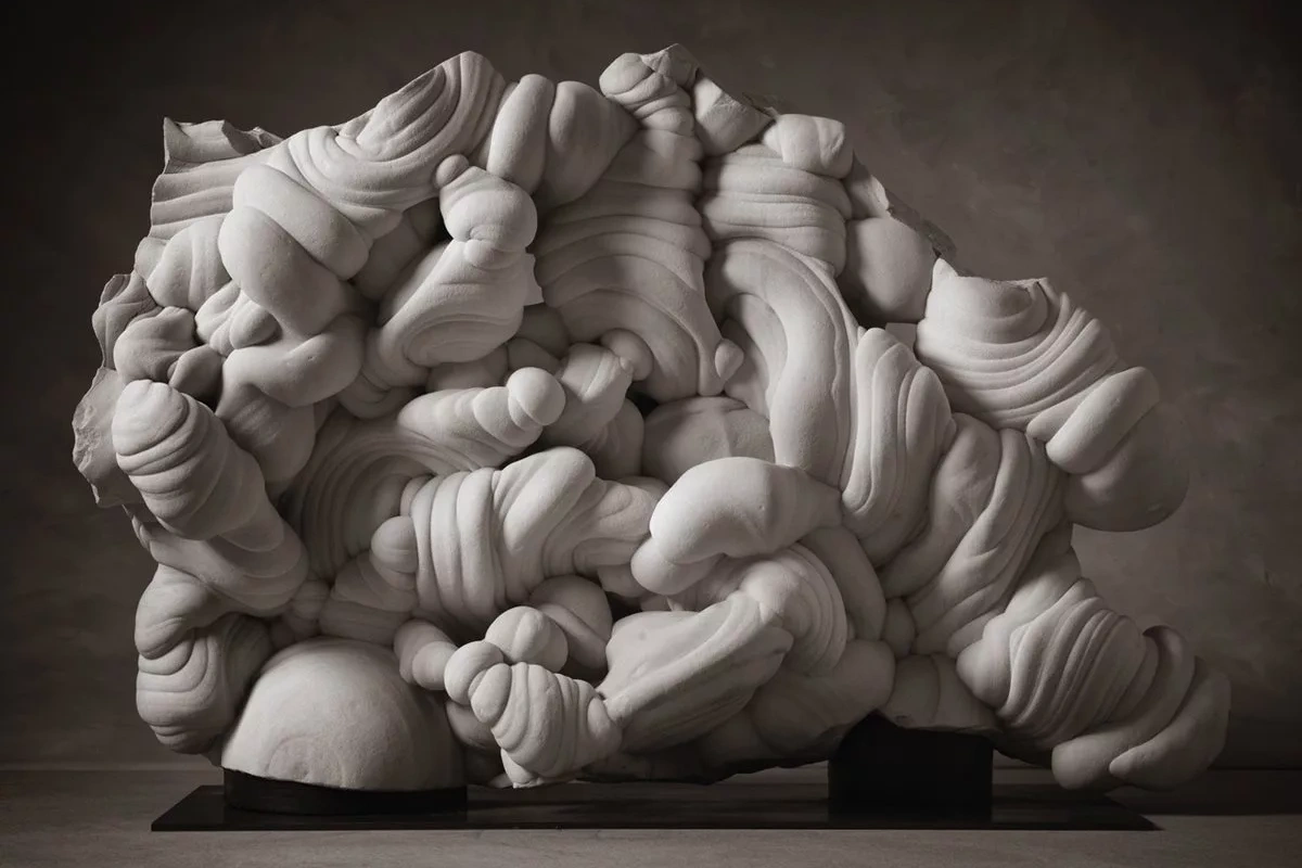 A naturally formed gogotte sandstone concretion from the Forest of Fontainebleau, its flowing white folds and curves resting on a dark surface