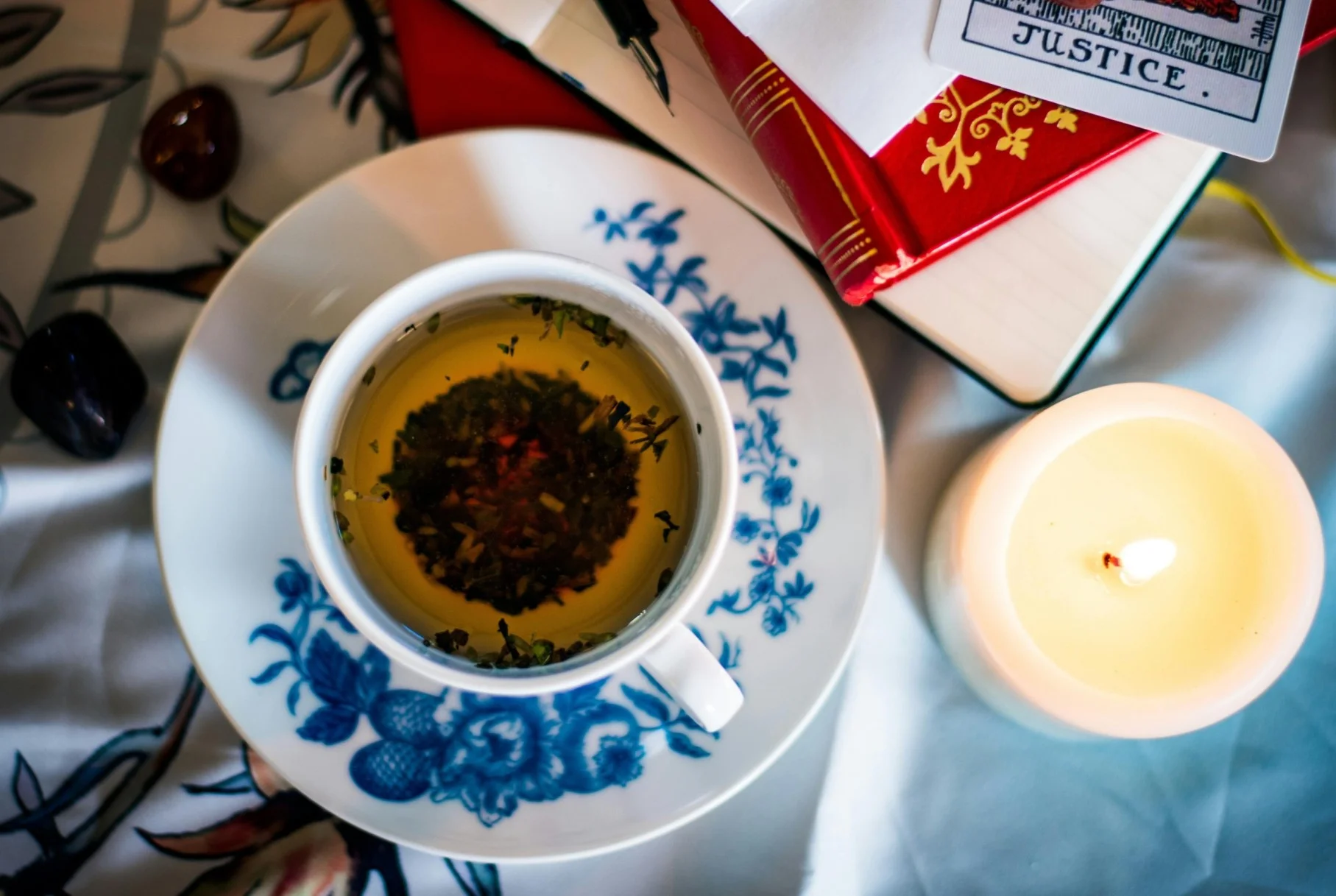 A white teacup with loose tea leaves settled around the rim, on a saucer in warm window light