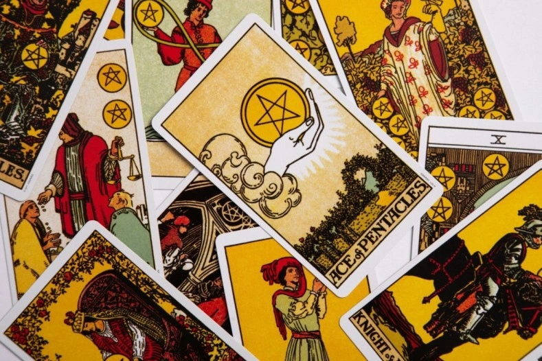 The Major Arcana cards of a tarot deck fanned face-down on dark linen, with a single card (The Star) turned face-up at the centre, beside a small white candle and a piece of clear quartz, photographed in low ambient light