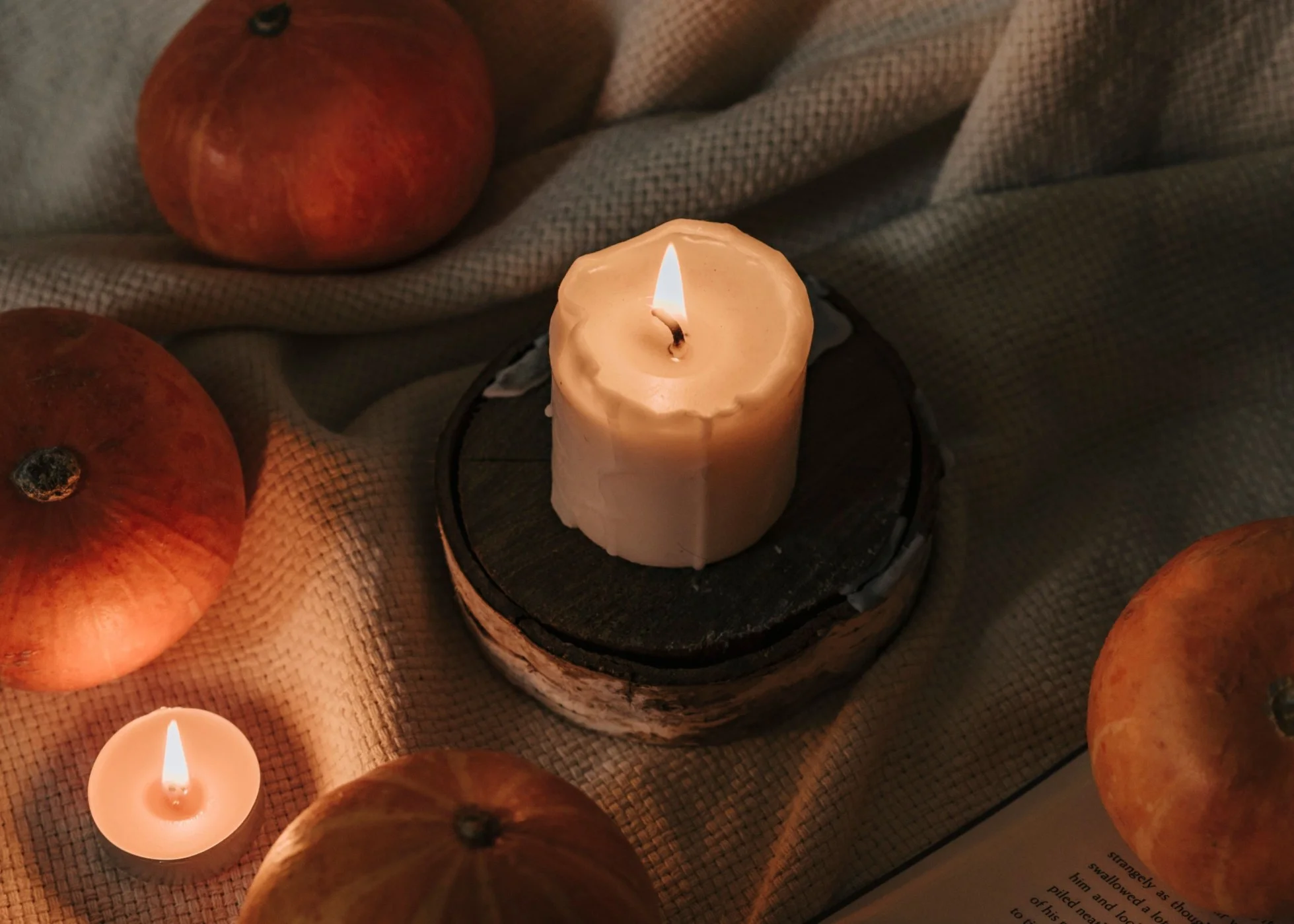 A single white candle on a windowsill at midnight on Samhain, beside a carved pumpkin lit from within, a small bowl of water for the ancestors, and an open journal with handwritten intentions, photographed in low warm light