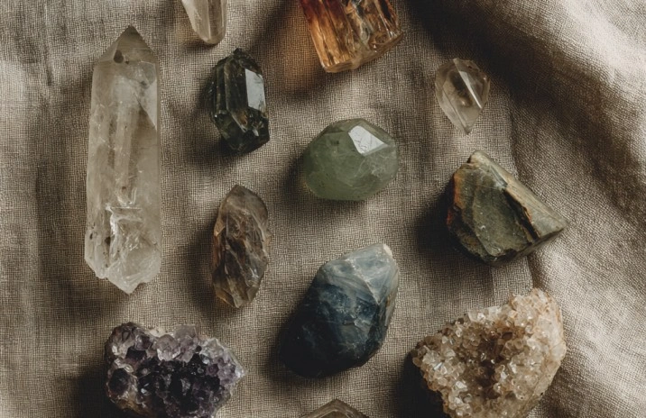 A flat lay of raw and tumbled crystals (including amethyst, citrine, fluorite and rough quartz) arranged on tan linen