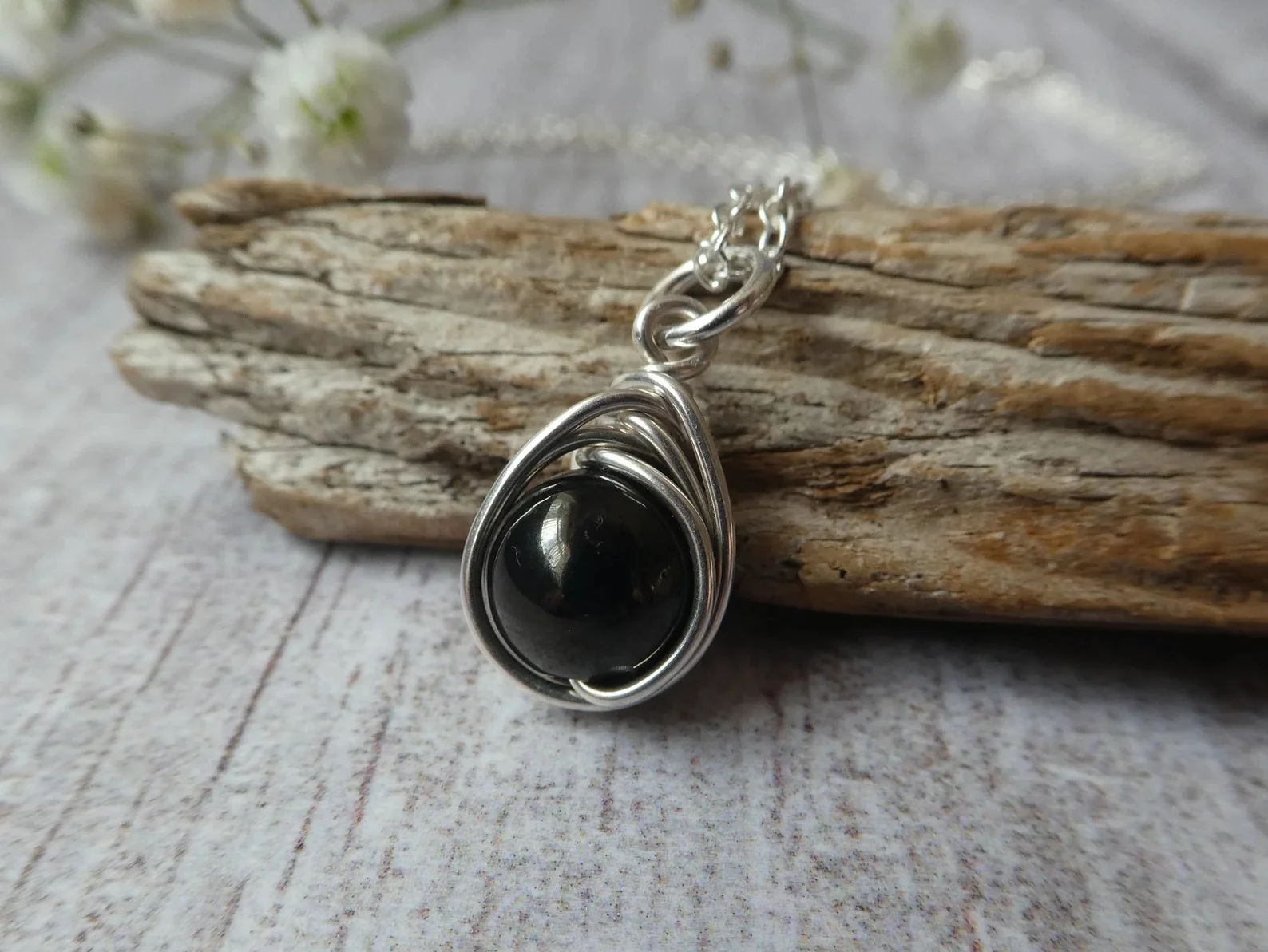 A polished black piece of Whitby jet resting on weathered grey stone beside a raw unpolished fragment, photographed in soft daylight that shows the deep brown-black sheen