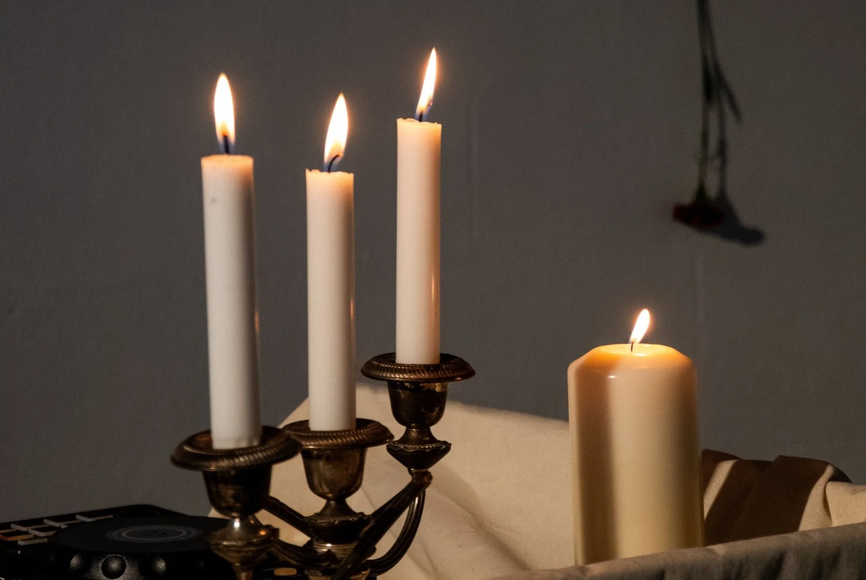 A single white candle burning on a windowsill at dusk beside a small framed photograph laid face up, a sprig of dried rosemary, and a cup of tea left untouched, photographed in low autumn light